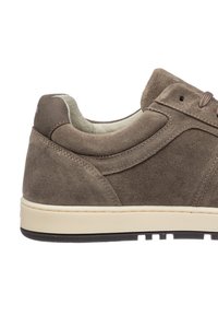 Brown suede sneaker with a low profile, padded ankle collar, and cream rubber sole. Features tonal stitching and subtle branding on the heel.