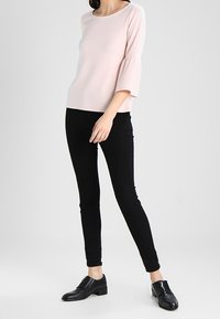 Světlé růžové tričko s krátkým rukávem a rozšířenými manžetami, spárované s černými skinny džíny a černými oxfordkami se zipem na boku.