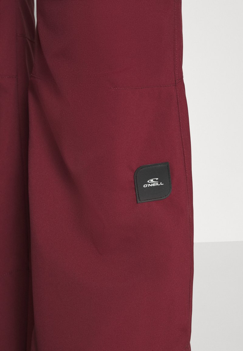 Bordowe spodnie narciarskie wykonane z wytrzymałego materiału, z małą czarną metką logo O'Neill i gładką, matową fakturą.