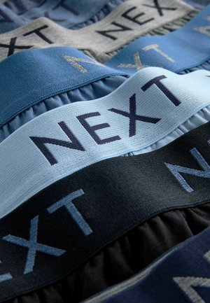 Textilband i nyanser av blått, grått och svart med ordet "NEXT" i kontrasterande broderade bokstäver och en veckad struktur.