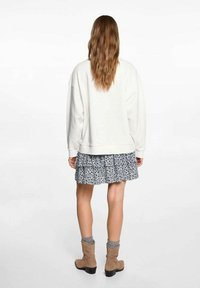 Kerman värinen oversized huppari, kerrostettuna musta-valkoisen kukkaroimalta hameen päälle, yhdistettynä vaaleanruskeisiin nilkkureihin ja harmaisiin sukkiin.