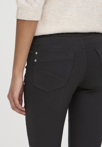 Jean slim negro con diseño de cinco bolsillos, que presenta dos bolsillos traseros con un sutil patrón de costura y mínimos acentos de metal.