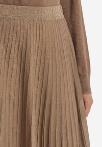 Plisserad kjol i metallisk taupe-tyg med en texturerad yta. Midjan är elastisk och har en subtil lyster genom hela designen.