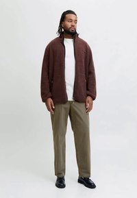 Brown fleece jacket with a zip, featuring side pockets, paired with a white t-shirt and olive green pants, completed with black shoes.