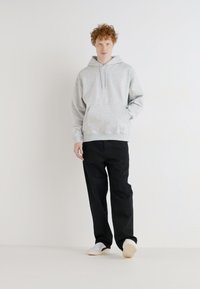 Sweat à capuche gris clair, coupe décontractée, fabriqué en matériau doux. Associé à un pantalon noir ample et des baskets blanches.