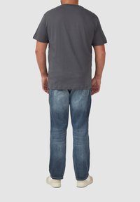 Graues Kurzarm-T-Shirt mit rundem Ausschnitt, kombiniert mit mittelblauen Jeans und weißen Turnschuhen, von hinten betrachtet.