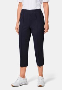 Marine blauwe cropped broek van een gestructureerde stof, met een elastische tailleband en zijkanten, gecombineerd met witte sneakers.