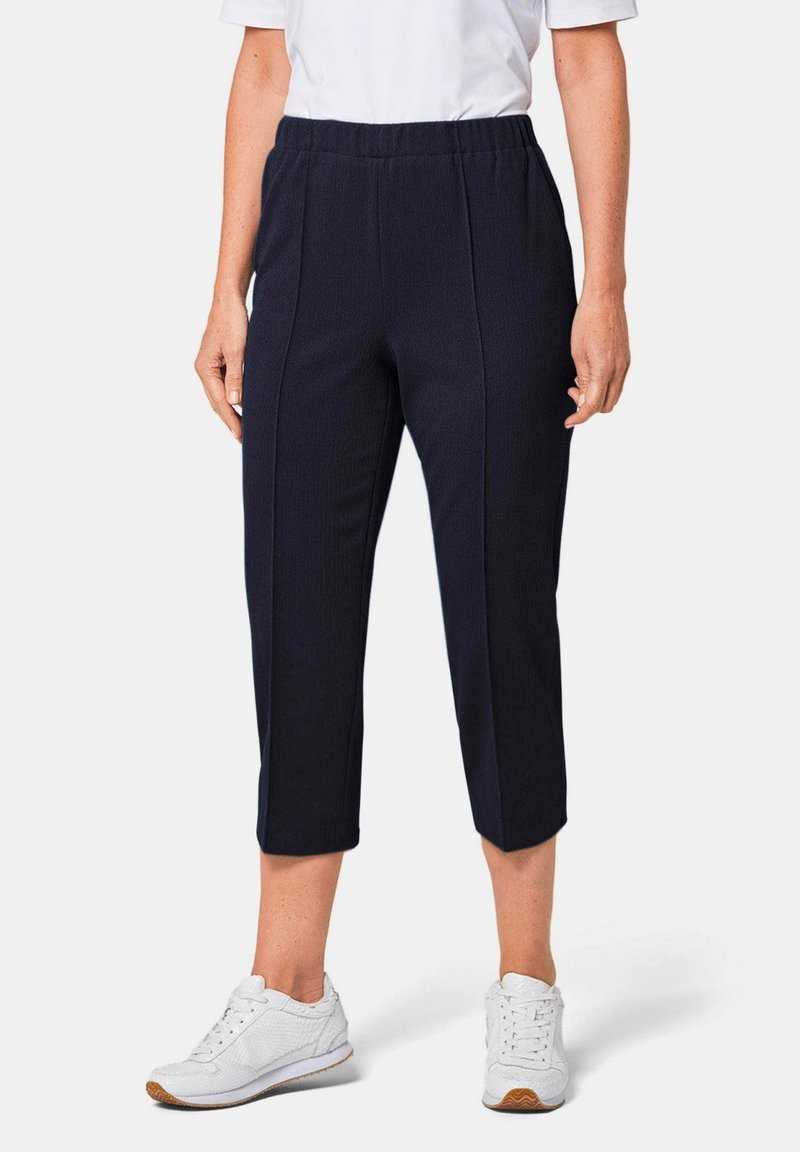 Marine blauwe cropped broek van een gestructureerde stof, met een elastische tailleband en zijkanten, gecombineerd met witte sneakers.