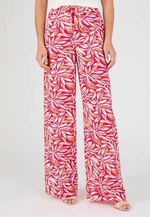 Pantaloni rosa a gamba larga con motivo di foglie bianche e arancioni, vita elastica con laccio, indossati con sandali aperti nude.