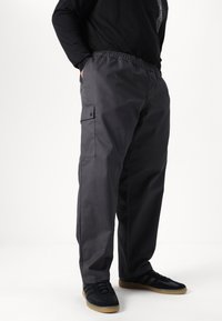 Grey cargo pants with an elastic waistband, side pockets, and a smooth texture, paired with black athletic shoes.