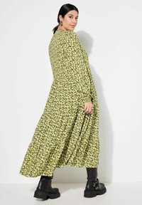 Vestido midi floral verde con mangas largas, diseño en capas y un patrón sutil. Combinado con botas negras hasta el tobillo y accesorios plateados.