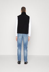 Czarna kamizelka z sztruksu z wysokim kołnierzem, noszona na białej koszuli z długim rękawem. Dopełnieniem stroju są niebieskie dżinsy i czarne trampki.