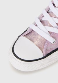 Zapatilla de lona morada con purpurina, cordones blancos, puntera de goma y suela texturizada. Acentos negros a lo largo de la puntera y el sistema de cordones.