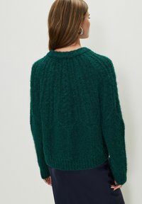 Túlméretezett zöld pulóver, texturált kötött anyagból, bordás gallérral és szegéllyel, laza szabással és hosszú ujjakkal.