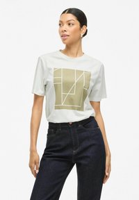 Vit kortärmad t-shirt med en geometrisk olivgrön grafik på framsidan. Kombinerad med mörka högmidjade jeans. Klara linjer.