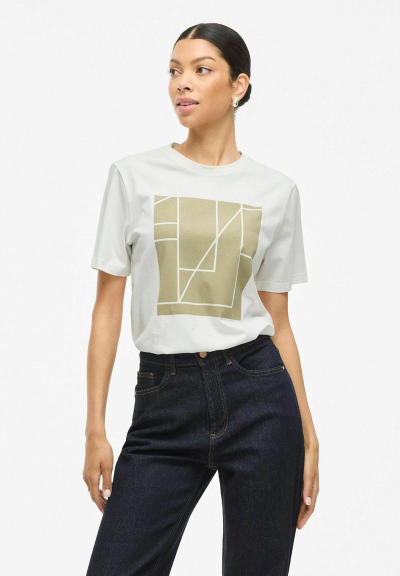 Vit kortärmad t-shirt med en geometrisk olivgrön grafik på framsidan. Kombinerad med mörka högmidjade jeans. Klara linjer.