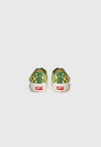 Green and yellow checkered slip-on shoes with white soles and red logo detail on the heel. Textured fabric upper and rounded design.