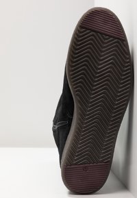 Black suede shoe sole with a textured, zigzag pattern; features a maroon accent on the heel and a side zipper detail.
