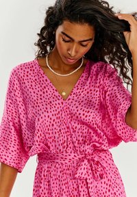 Růžové šaty s červenými puntíky, výstřih do V, volné rukávy, stažený pas se zavazováním. Hladká látka, jemně se přizpůsobuje tělu.