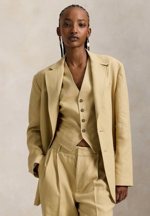 Σύνολο μπεζ λινό που περιλαμβάνει μακρύ σακάκι, εφαρμοστό γιλέκο με κουμπιά και παντελόνια φαρδιάς γραμμής. Ύφασμα με υφή σε ουδέτερο τόνο.