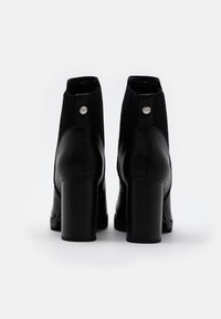 Botas negras de tobillo con una parte inferior de cuero y una parte superior de tejido de punto. Tacón cuadrado y botones metálicos decorativos en la parte posterior.