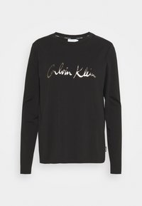 Svart långärmad skjorta i bomull, med en glansig silver "Calvin Klein"-logotyp över bröstet och rund halsringning.