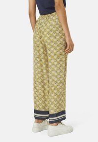 Pantaloni larghi di colore giallo con dettagli blu scuro all'orlo. Vita elastica, con un design floreale che presenta elementi blu e bianchi.