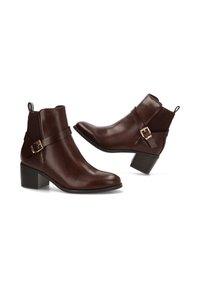 Botas de piel marrón hasta el tobillo con punta afilada, tacón bajo y bloque, y correa decorativa con detalles en tono dorado. Textura suave, diseño moderno.