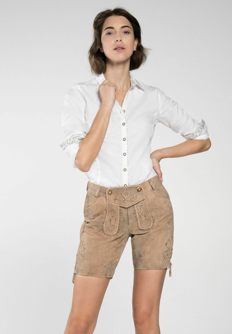 Bruine suede shorts met geborduurde bloemdetails, knoopaccenten en een hoge tailleband, gecombineerd met een witte blouse met kraag en decoratieve manchetten.