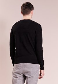 Musta neulepusero, jossa on teksturoidut vaakasuorat kuviot, pitkät hihat ja pyöreä pääntie. Yhdistetty vaaleanharmaisiin housuihin.