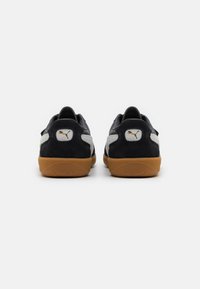 Mustat mokkanahka sneakersit, joissa on kuminen pohja, harmaat sivupaneelit ja valkoinen logopatchi kantapäällä. Klassinen matala design.