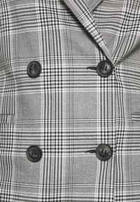 Dubbelt knäppt kavaj i ett svart- och vitt rutmönster. Utrustad med svarta knappar, strukturerade kragar och textil med textur.