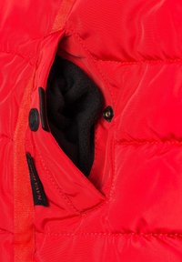 Rød polstret jakke med en sort fleece-foret lomme med trykknaplukning. Synlig syning og tekstureret stofdetalje.