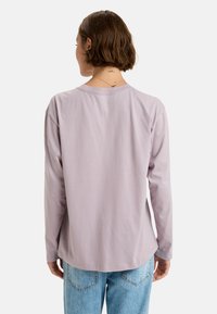 Långärmad lavendelfärgad T-shirt i mjuk bomull, med rund halsringning och avslappnad passform, tillsammans med ljusblå denimjeans.