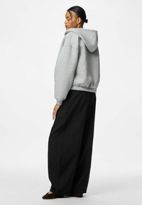 Felpa grigia con cappuccio, spalle scese, polsini e orlo a costine, abbinata a pantaloni larghi neri. Modello visto di lato.