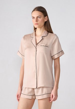 Set de pijamale din mătase roz deschis, compus dintr-o bluză cu nasturi și mâneci scurte, cu detalii negre, și o pereche asortată de pantaloni scurți.
