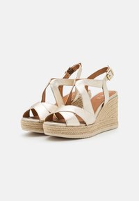 Sandali wedge metallici dorati con cinturini incrociati, design peep-toe, suola intermedia in corda intrecciata e fibbia per caviglia regolabile.