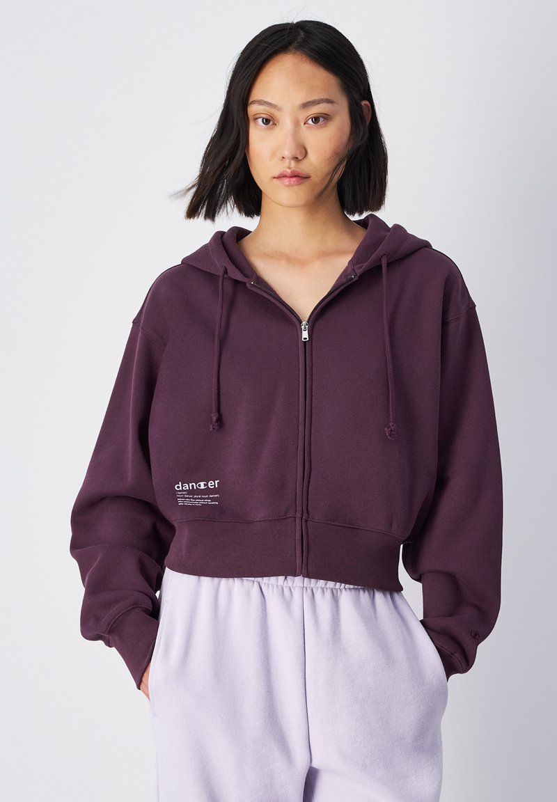 Felpa corta viola con cappuccio, coulisse, zip frontale e tasche laterali. Presenta una stampa del logo sul lato sinistro e orlo a costine. Tessuto morbido.