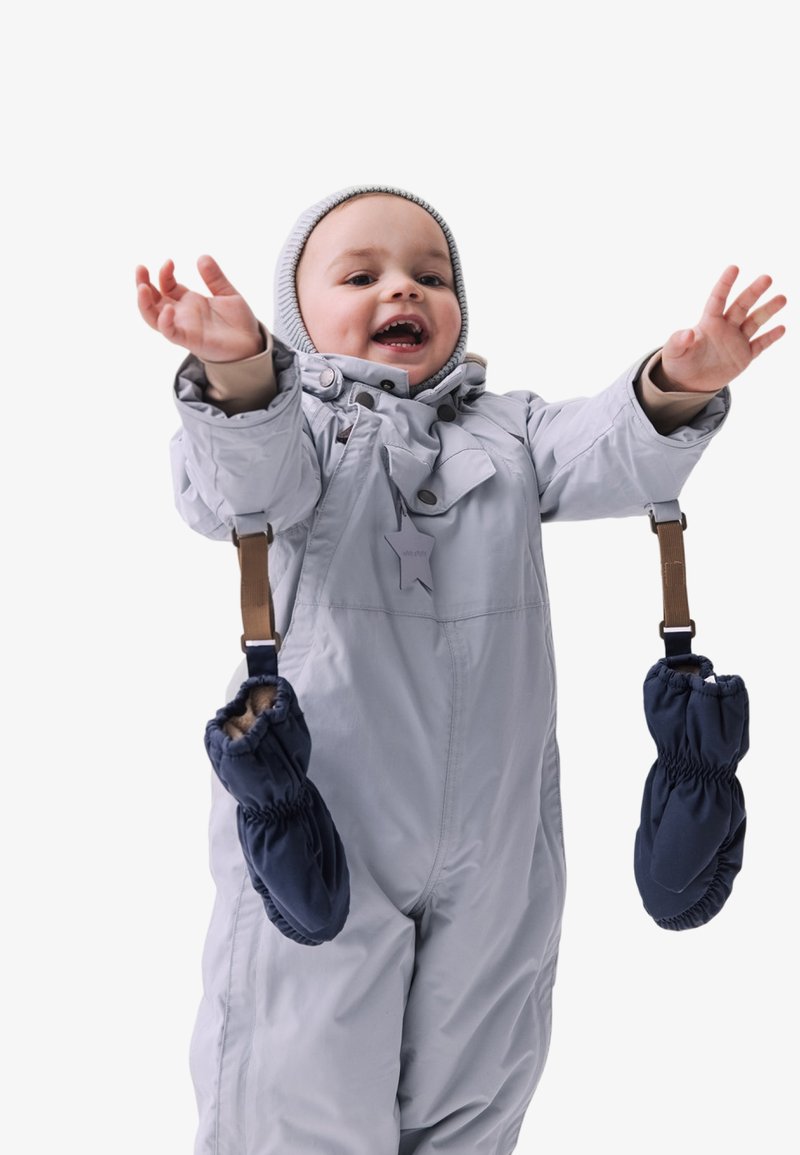 Grau isolierter Schneeanzug mit Kapuze, ausgestattet mit braunen Riemen, die marineblaue Handschuhe an den Handgelenken halten. Glatte Textur und funktionale Details sind offensichtlich.