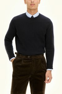 Granatowy sweter dzianinowy z okrągłym dekoltem, noszony na jasnoniebieskiej koszuli z kołnierzykiem, w połączeniu z brązowymi spodniami corduroy z kieszeniami bocznymi i guzikiem.