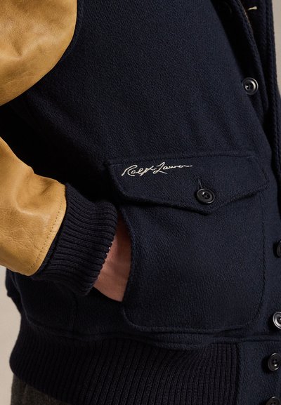 Ναυτικό σακάκι από μείγμα μαλλιού με καφέ δερμάτινα μανίκια, ραμμένο γιακά και μπροστινές τσέπες που διαθέτουν κεντημένο λογότυπο "Ralph Lauren". Ορατές κουμπότρυπες.