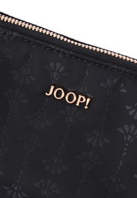 Borsa in tessuto nero con motivo floreale, logo "JOOP!" in tono oro e chiusura con zip. Superficie testurizzata con una leggera lucentezza.