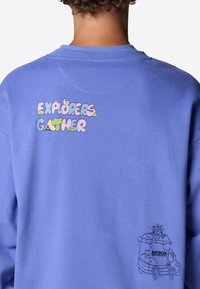 Sudadera azul con el colorido texto "EXPLORERS GATHER" en la parte posterior y un dibujo en línea negra de un camión con un logotipo y un remolque.