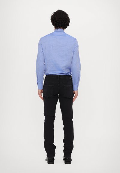 Blau gestreiftes Langarmhemd, schmal geschnitten, kombiniert mit schwarzen Jeans. Das Hemd hat einen geknöpften Kragen und einen Rückensteg, die Jeans haben einen klassischen Schnitt.