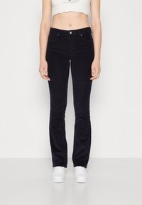 Marineblauwe flared corduroypantalons hebben een hoge taille, zijzakken en een knoopsluiting. Gepaarde met witte sneakers voor een casual look.