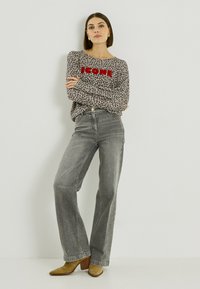 Top de manga larga estampado de leopardo con texto rojo "ICON", combinado con jeans de pierna ancha de talle alto en gris y tacones color canela.