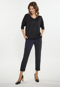 Musta, pitkähihainen, V-kaula-aukkosweateri, jossa on vaakasuorat metallinväriset raidat, yhdistettynä slim-fit mustiin housuihin ja mustiin korkokenkiin.