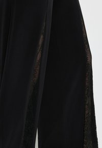 Schwarze Hosen mit durchsichtigen Spitzen-Seitenbahnen im Blumendesign. Der glatte Stoff kontrastiert mit der strukturierten Spitze und schafft einen schichtigen Look.