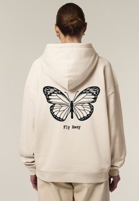 Felpa con cappuccio color crema caratterizzata da un grande grafico di una farfalla nera e la scritta "Fly Away" sul retro. Tessuto morbido, vestibilità ampia.