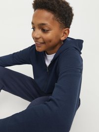 Sudadera con cremallera de color azul marino y pantalones a juego, fabricados en tejido suave. Presenta una cremallera frontal y un corte relajado, adecuado para el uso casual.